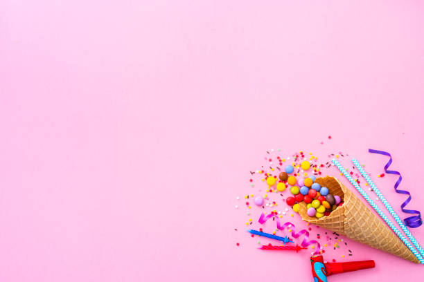 Party, birthday or carnival backgrounds. Overhead view of multi colored items like confetti, candies, drinking straws and streamers shot at the right of pink background leaving useful copy space for text and/or logo. High resolution 42Mp studio digital capture taken with SONY A7rII and Zeiss Batis 40mm F2.0 CF lens