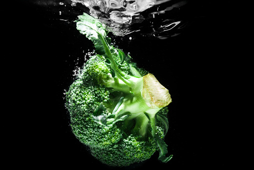 Fresh green broccoli dropped into water isolated on black background