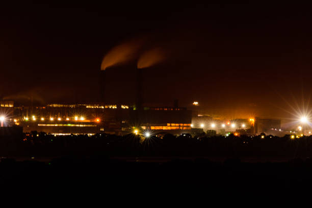 vue sur les lumières de la ville la nuit. la fumée des cheminées de l’usine monte vers le ciel. concept de pollution de l’environnement - factory night skyline sky photos et images de collection