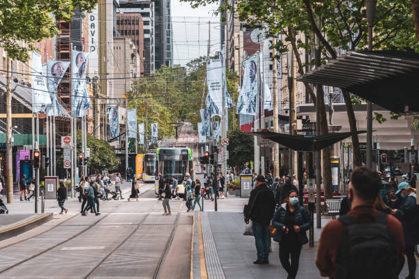 A Public Transport Victoria tram is on Bourke Street while pedestrians cross the road Melbourne, Victoria, Australia, October 23, 2021: A Public Transport Victoria tram is on Bourke Street while pedestrians cross the road at the intersection of Swanston Street. melbourne street crowd stock pictures, royalty-free photos & images