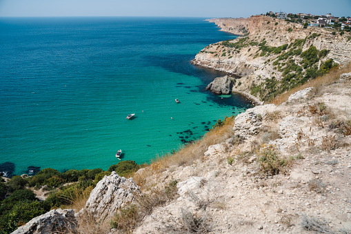 Boats and yachts in the crystal clear azure sea on a sunny day. Cape Fiolent in Sevastopol. The concept of an ideal place for summer travel and relaxation.
