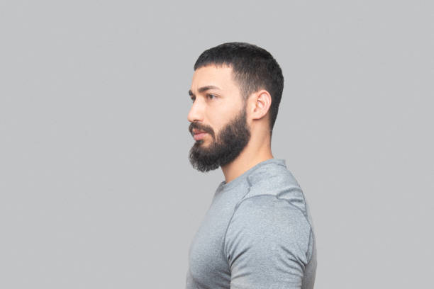Profile view of a young man looking away over gray background. Horizontal shot.