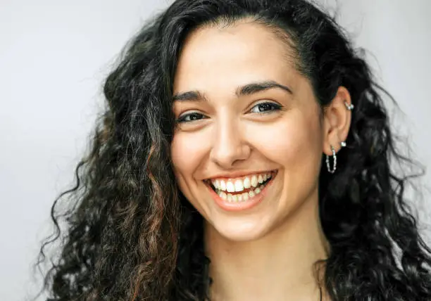 Close-up portrait of cheerful young woman with earrings. Smiling female with curly black hair.