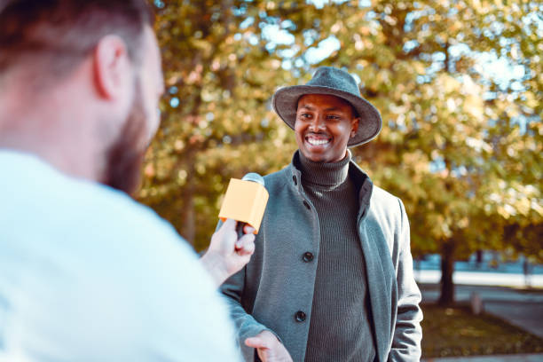 lächelnder afrikanischer mann, der vorbeikommt und schnelle journalistenumfrage gibt - recorded outdoors stock-fotos und bilder