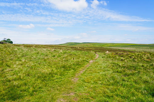 Barely visible winding footpath crosses the Derbyshire hills under a cloudy blue sky