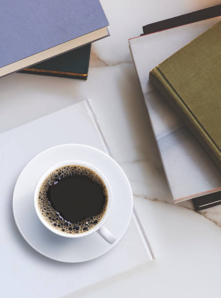 istock Flat lay of black coffee in ceramic cup on white book with various old textbooks stacks on marble tabletop 1348965545