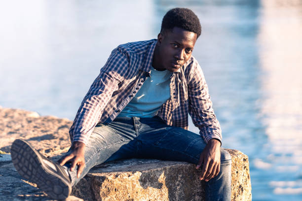 istock African young man posing facing the camera while sitting next to a river 1348965904
