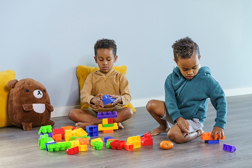 Two cute preschool age black boys sit on the floor and build with large colorful plastic toy blocks. The creative and curious children are having fun at school or daycare. Learning, school, child care and family concepts.