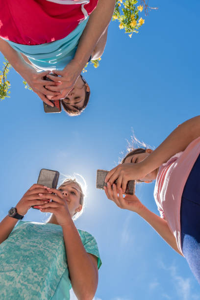 istock Three young women seen from below while looking at their smartphones with the sun above them. 1348968345