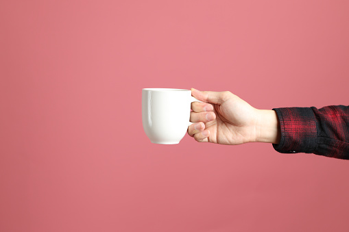 The Asian man hand holding mug to give for someone on the pink background.