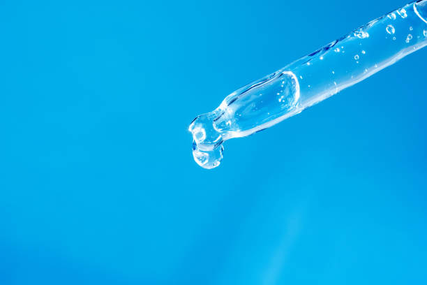 istock Glass pipette with facial serum, bubbles inside and falling drop on light blue background macro. Modern cosmetic product advertising. Medical research, innovation concept. Dropper with gel closeup 1348968463