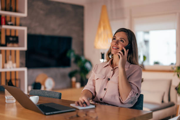 istock Smiling woman talking on phone at home office. 1348975341