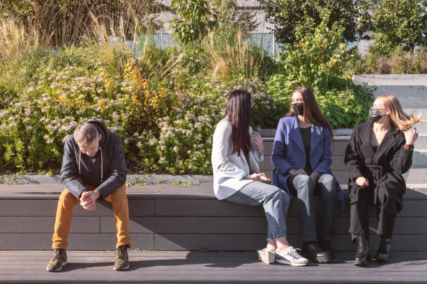 istock Friends with face masks talking and sitting on bench 1348976926