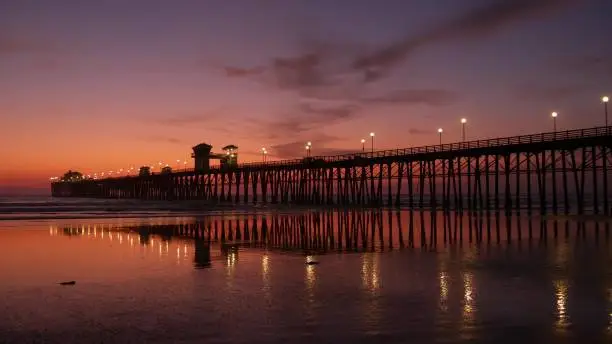 Photo of Pier silhouette Oceanside California USA. Ocean tide tropical beach. Summertime gloaming atmosphere.