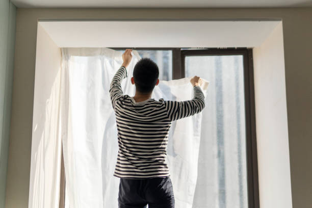 istock Asian man hanging curtains with protective face mask  while moving house 1348982056