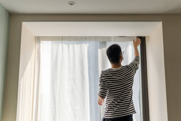 istock Asian man hanging curtains with protective face mask  while moving house 1348982104
