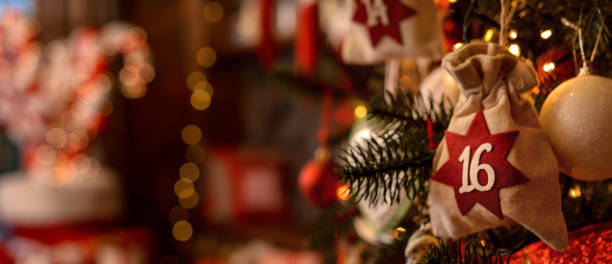 christmas background. advent calendar. advent calendar in the form of an eco bag hangs on the christmas tree against the background of the christmas room with a fireplace and santa's boots. - advent imagens e fotografias de stock