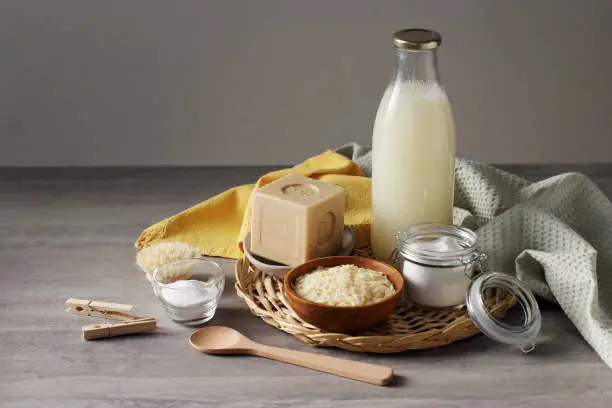 Photo of Traditional hard soap bar, pure soap flakes, baking soda and home made washing up liquid in the glass bottle. DIY making home-made laundry detergent.