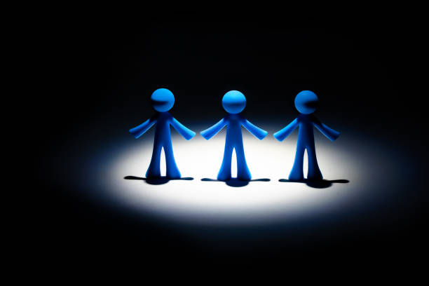 istock Three symbolic male figures in a circle of light on a black background 1348990874