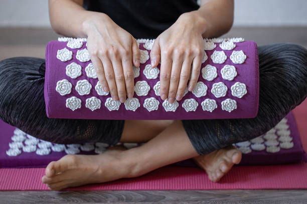 Purple massage acupuncture pillow and white massage tips in female hands. Close up massage acupuncture mat with pillow and white massage tips, massage mat for relaxation and treatment. acupuncture mat stock pictures, royalty-free photos & images