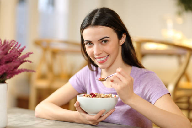 mujer feliz comiendo cereales mirándote - women spoon tasting elegance fotografías e imágenes de stock