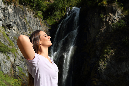 Relaxed woman breathing fresh air and resting in a waterfall