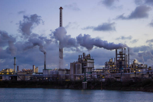 fabric and factory buildings at the rhine harbour at dawn. Some reflections in the water. Smoking chimneys in frot of a blue dark sky.