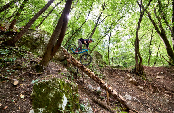 Enduro biker at the top of a challenging drop on a self-constructed trail in the woods with sunlight peeking through Enduro bike with full suspension and protective sports gear and equipment on a steep hill on a dirt path sports photography stock pictures, royalty-free photos & images