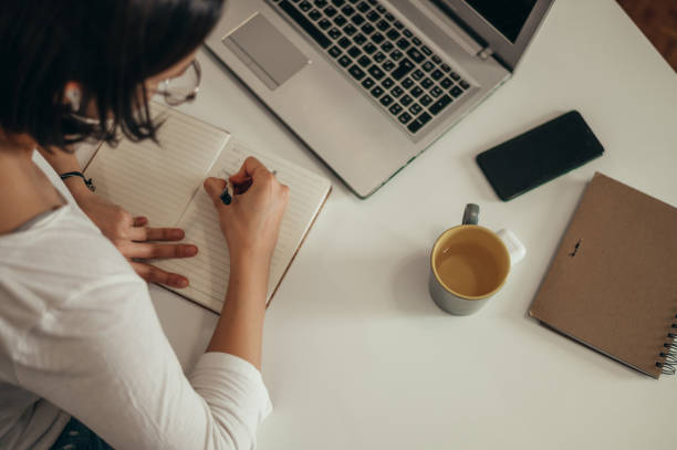 istock Woman writing in a notebook and using a laptop while working from home 1349010562