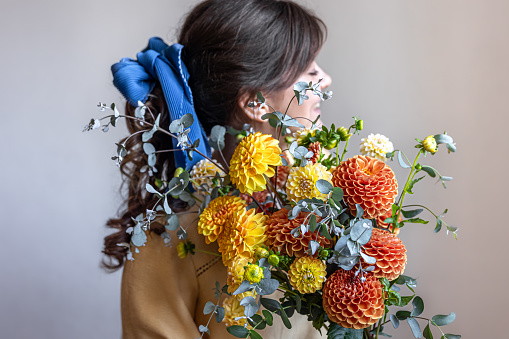 Young woman with a blue ribbon in her hair, holding a bouquet of yellow and orange chrysanthemums, gray background.