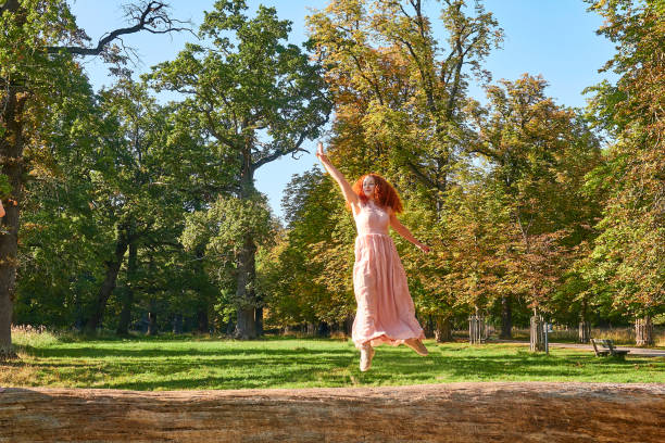 Red haired beautiful  woman jumping on a trunk, summer sun