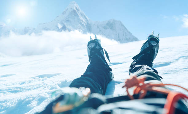 pov-aufnahme der verzögerungen eines bergsteigers in steigeisen. er liegt und ruht auf einem schneeeisfeld mit ama dablam (6812m) gipfel, der mit wolken bedeckt ist. extremal people urlaubskonzept - himalayas mountain climbing nepal climbing stock-fotos und bilder