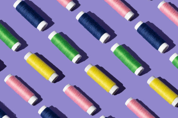 istock sewing thread in pink yellow, green and blue color . minimal pattern concept on purple background. 1349017073