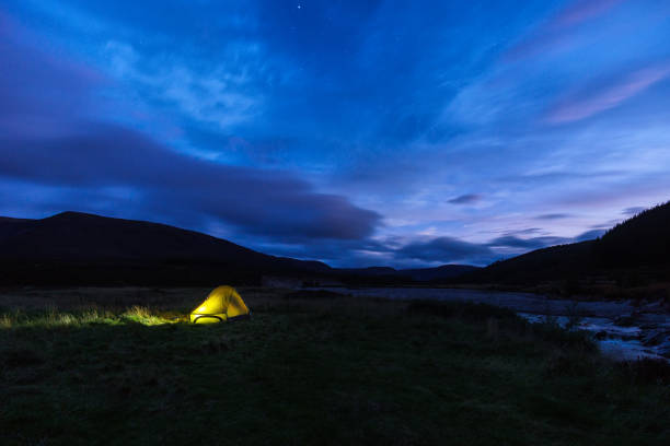 istock illuminated tent on meadow besides a river under a cloudy sky with star during blue hour, Scotland 1349018166