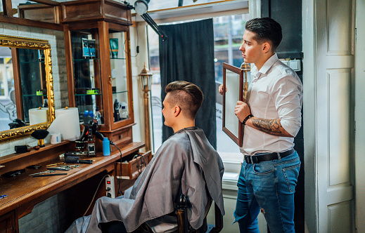 Young cheerful man looking at himself in the mirror at barbershop satisfied with his new hairstyle