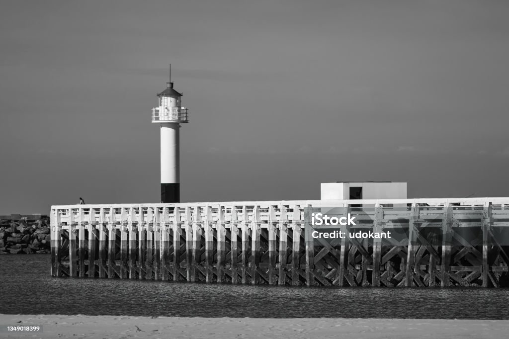 Alone by the lighthouse Solitary figure on a pier with a lighthouse along the coast Black And White Stock Photo
