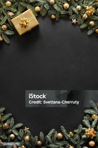 istock Christmas vertical frame with golden gift, baubles, evergreen branches on black background. Xmas greeting card. 1349023797