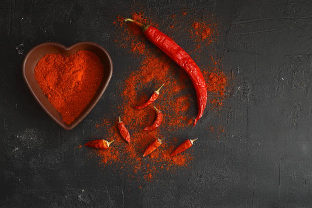 red hot chili peppers pó em tigela em forma de coração sobre a mesa de pedra preta. conceito de amor. vista superior plana lay com espaço de cópia - chilli powder - fotografias e filmes do acervo
