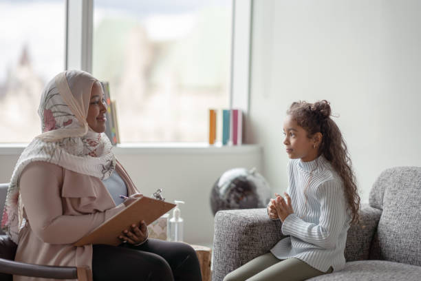 At Home Learning A Muslim Mother sits with her daughter as she teaches her from the comfort of their own home.  The young girl is seated on a sofa while the mother sits across from her on a chair with a clipboard in her hands.  She is testing the young girls memory and recording her answers. literacy photos stock pictures, royalty-free photos & images