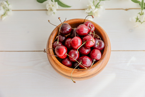 Fresh juicy red sweet cherry berries in the wooden bowl on light background in summer. Concept of healthy nutrition in tableware made of natural harmless material.