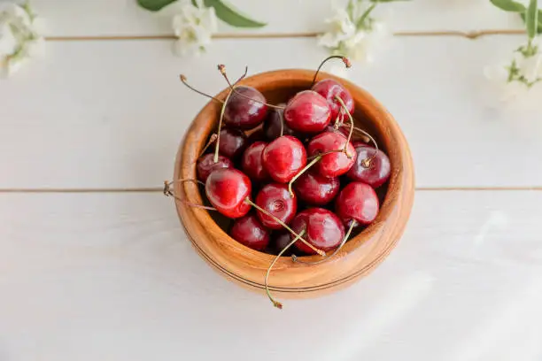 Photo of Fresh juicy red sweet cherry berries in the wooden bowl on light background in summer.