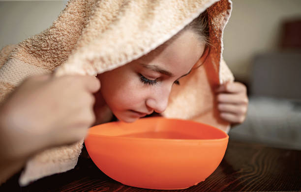 Little girl making inhalation with steamed aromatic water from the bowl stock photo