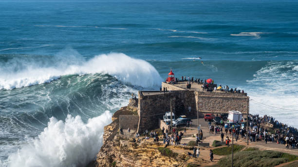 Giant Waves Breaking in Nazare, Portugal, Famously Known for Having the Largest Waves in the World Giant waves breaking near the historic Fort of Sao Miguel Arcanjo Lighthouse in Nazare, Portugal. Nazare is famously known for having the biggest waves in the world. nazare surf stock pictures, royalty-free photos & images