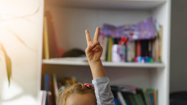 Front view of a schoolgirl raising her hand to answer the teacher’s question. stock photo