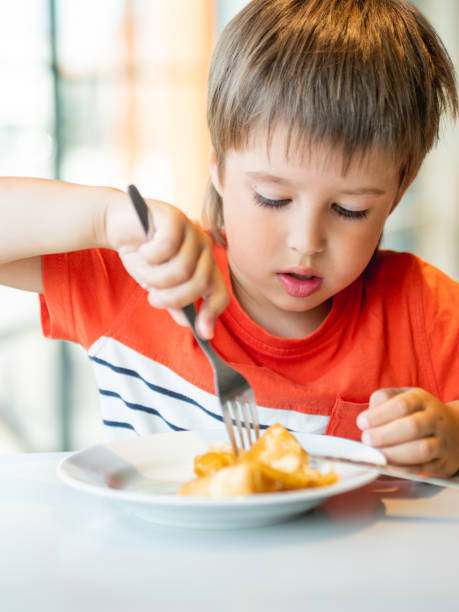 istock Cute kid in red t-shirt eats pancakes with knife and fork. Curious boy with funny expression on face. Tasty pastry for breakfast. 1349034232