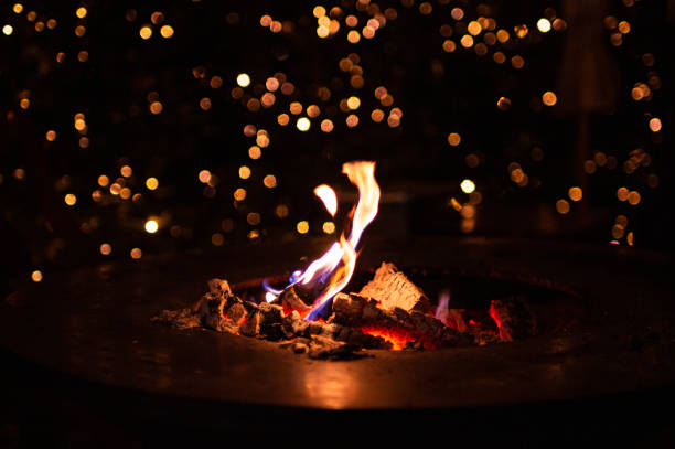 close up of fireplace with burning fire wood in cold winter night and bokeh christmas lights on traditional christmas market at Merano, South Tyrol, Italy close up of fireplace with burning fire wood in cold winter night and bokeh christmas lights on traditional christmas market at Merano, South Tyrol, Italy bonfire stock pictures, royalty-free photos & images