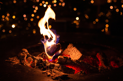 close up of fireplace with burning fire wood in cold winter night and bokeh christmas lights on traditional christmas market at Merano, South Tyrol, Italy