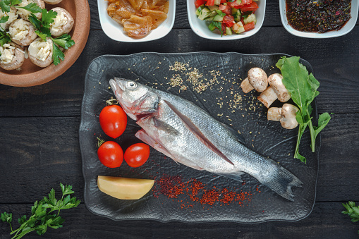 Fresh sea bass fish with herbs and lemon on a wooden cutting board