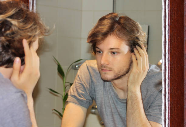 istock young man looking in the mirror,combing his hair,looking at problems on face 1349044206