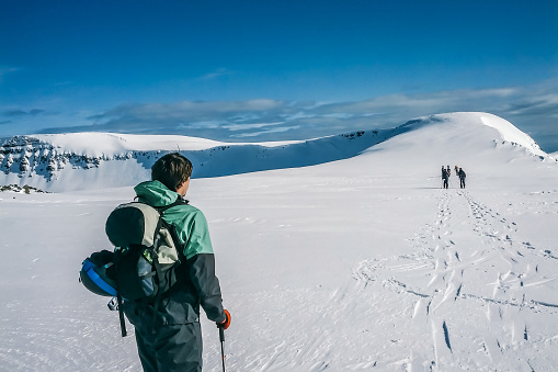 Mountaineering team starting a hike in the snowy mountains of Iceland. Man in green jacket admiring the beauty of the mountain before starting the trek.